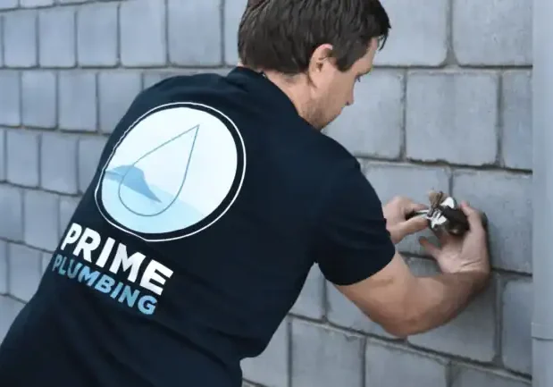 Plumber repairing outdoor faucet on brick wall